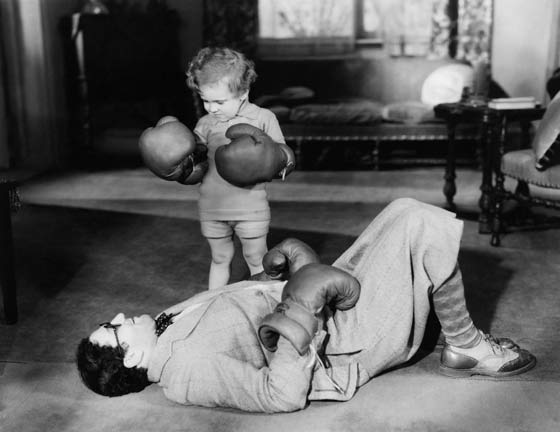 Photo en noir et blanc d'un petit garçon avec des gants de boxe qui a mis KO son père