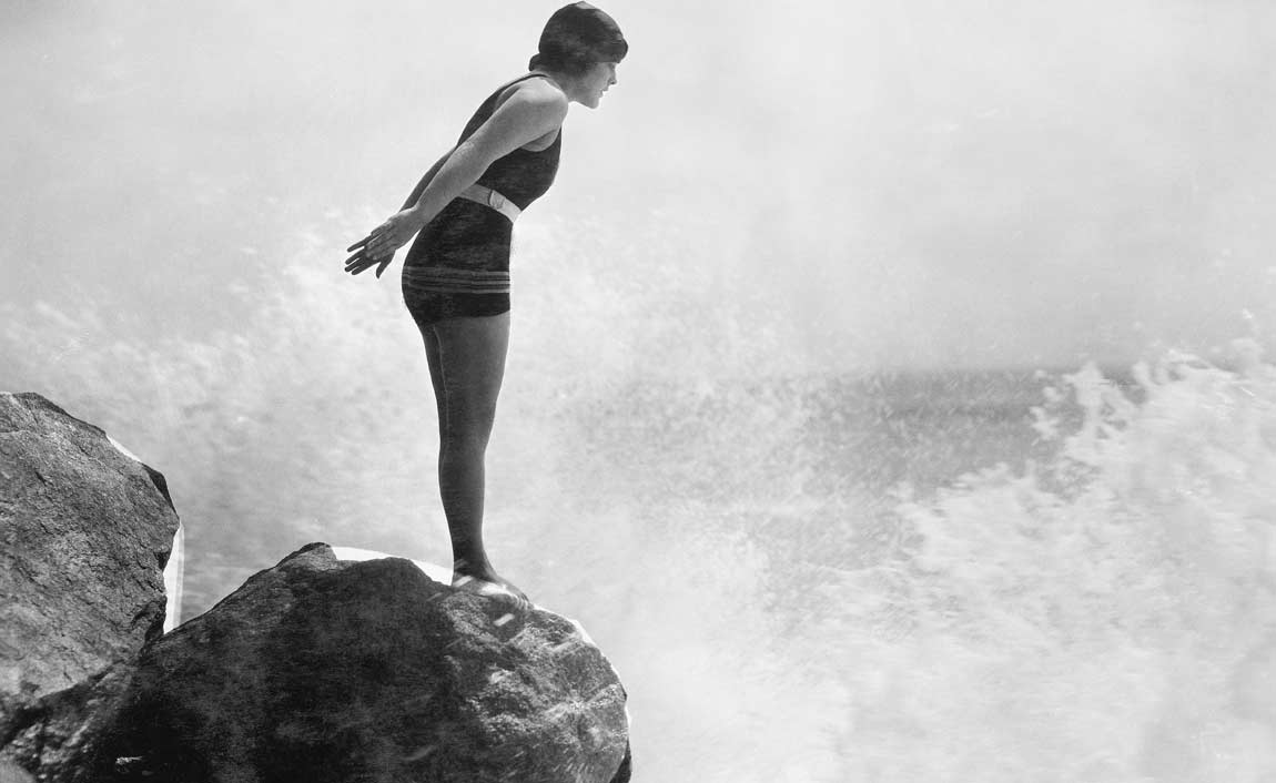 Photo noir et blanc d'une femme sur un rocher qui va plonger dans la mer