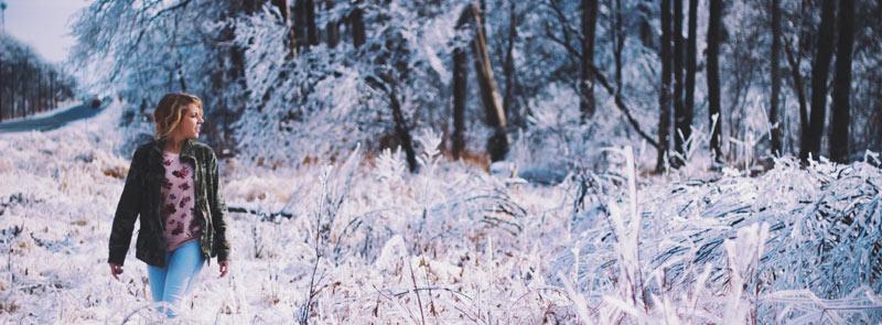 Photographie d'une femme se promenant en pleine nature en hiver, sous la neige