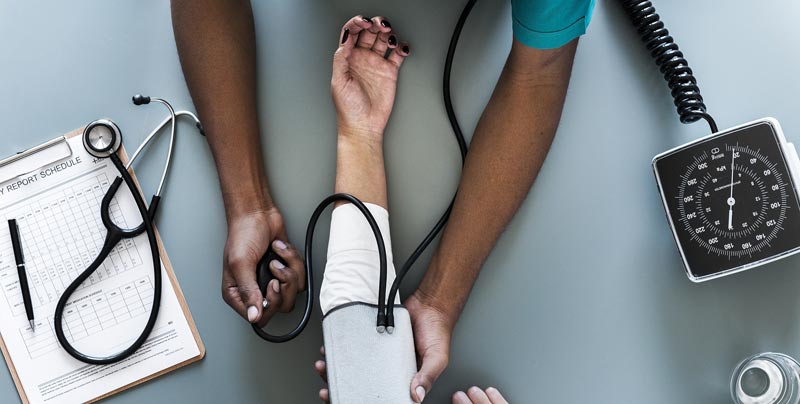 Photographie d'un infirmier noir professionnel de santé prenant la tension d'une patiente blanche, femme malade