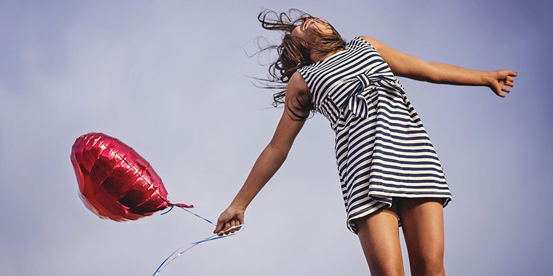 Photographie d'une jeune fille en bonne santé, habillée d'une robe rayée noir et blanche, sautant de joie et tenant dans sa main un ballon de baudruche rouge en forme de cœur, pour illustrer les bénéfices sur la santé d'un régime alimentaire comportant beaucoup d'aliments riches en fibres.