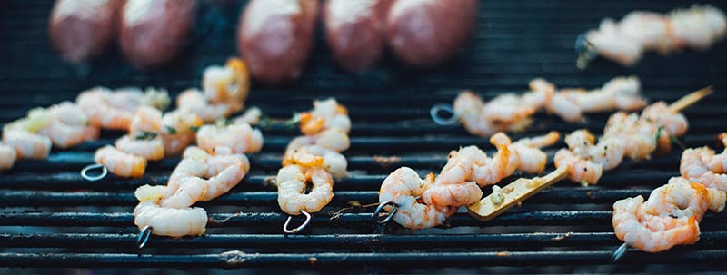 Crevettes et saucisses en train de griller sur un barbecue BBQ pour illustrer les dangers des protéines animales. Les régimes protéinés sont à éviter pour perdre du poids efficacement.