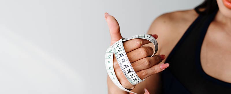 Femme qui tient dans sa main un mètre ruban pour illustrer les dangers de l'obsession de manger sain et de maigrir. Perdre du poids ne doit pas être une obsession.
