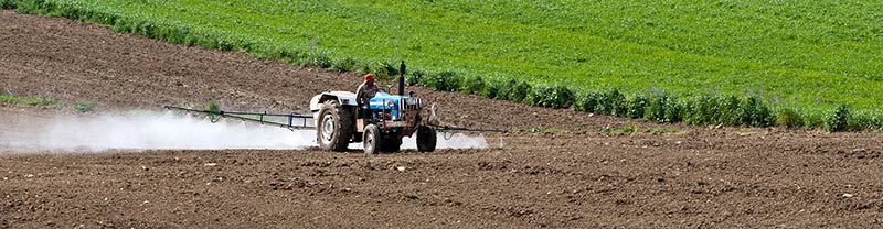 Photographie d'un agriculteur répandant des pesticides sur son champ nu à l'aide de son tracteur, ce qui est interdit pour les aliments bio
