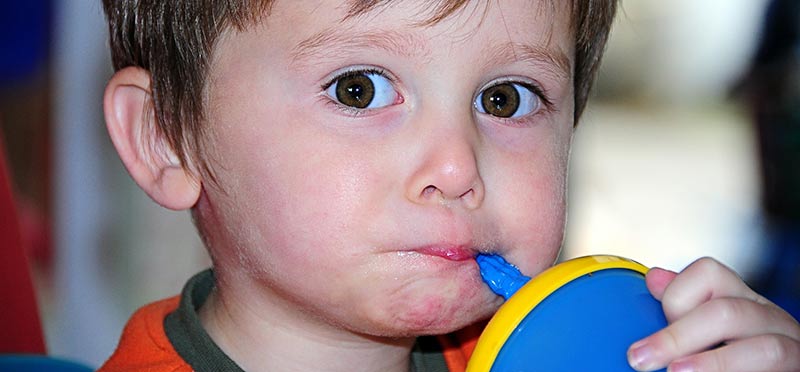 Photographie d'un enfant blanc en train de boire à une gourde bleue. L'éducation alimentaire permet de prémunir de l'obésité infantile.