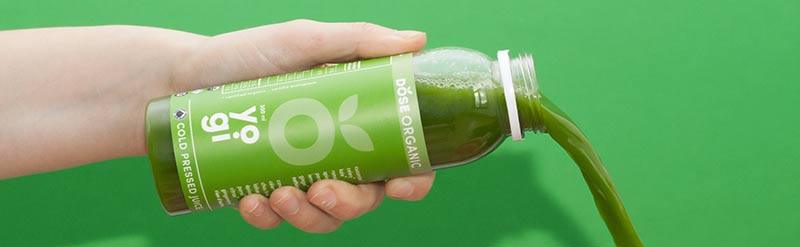 Photographie d'une personne en train de verser du jus vert (smoothie) sur un fond vert. Les aliments bio peuvent aussi être mauvais pour la santé s'ils sont industriels.