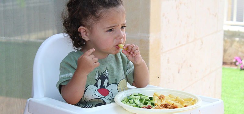 Éducation alimentaire : Photographie d'une petite fille assise dans une chaise haute Ikea blanche, qui prend son repas avec les mains