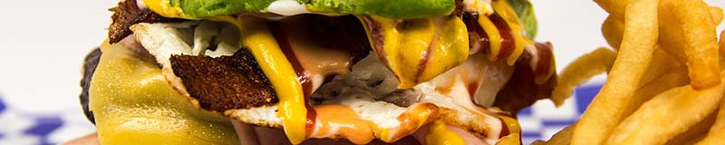 Gros plan d'un hamburger avec sauce, ketchup, mayonnaise, cheddar, bacon, frites... Les graisses peuvent causer des dommages au foie : NASH, maladie du soda, maladie du foie gras humain...