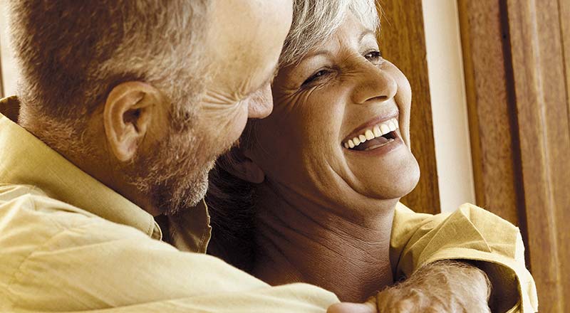 Photographie en teinte sépia d'un couple de senior enlaçés et heureux, souriants à pleine dents, joyeux d'avoir réussi à se débarrasser de l'arthrose et à ne plus avoir de douleurs dans leurs articulations grâce à des recettes simples, naturelles et sans effets secondaires.