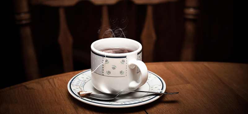 Le thé peut entraîner des carences nutritionnelles en fer en raison des tanins qu'il contient. Photographie d'une tasse de thé chaud fumant sur une table en bois.
