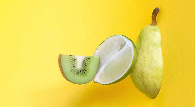 Photographie de trois fruits (kiwi, citron, poire) découpés sur un fond jaune pour illustrer le fait que les micronutriments sont essentiels à la santé et à la micronutrition.