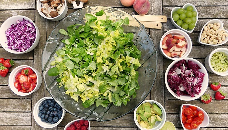 Micronutriments : photographie d'une salade verte dans un saladier entouré de petits bols contenant une grande variété des fruits et légumes frais et crus, framboise, fraise, betterave, raisin, champignons, chou rouge, fraise, myrtilles, pêche, avocat, citron.