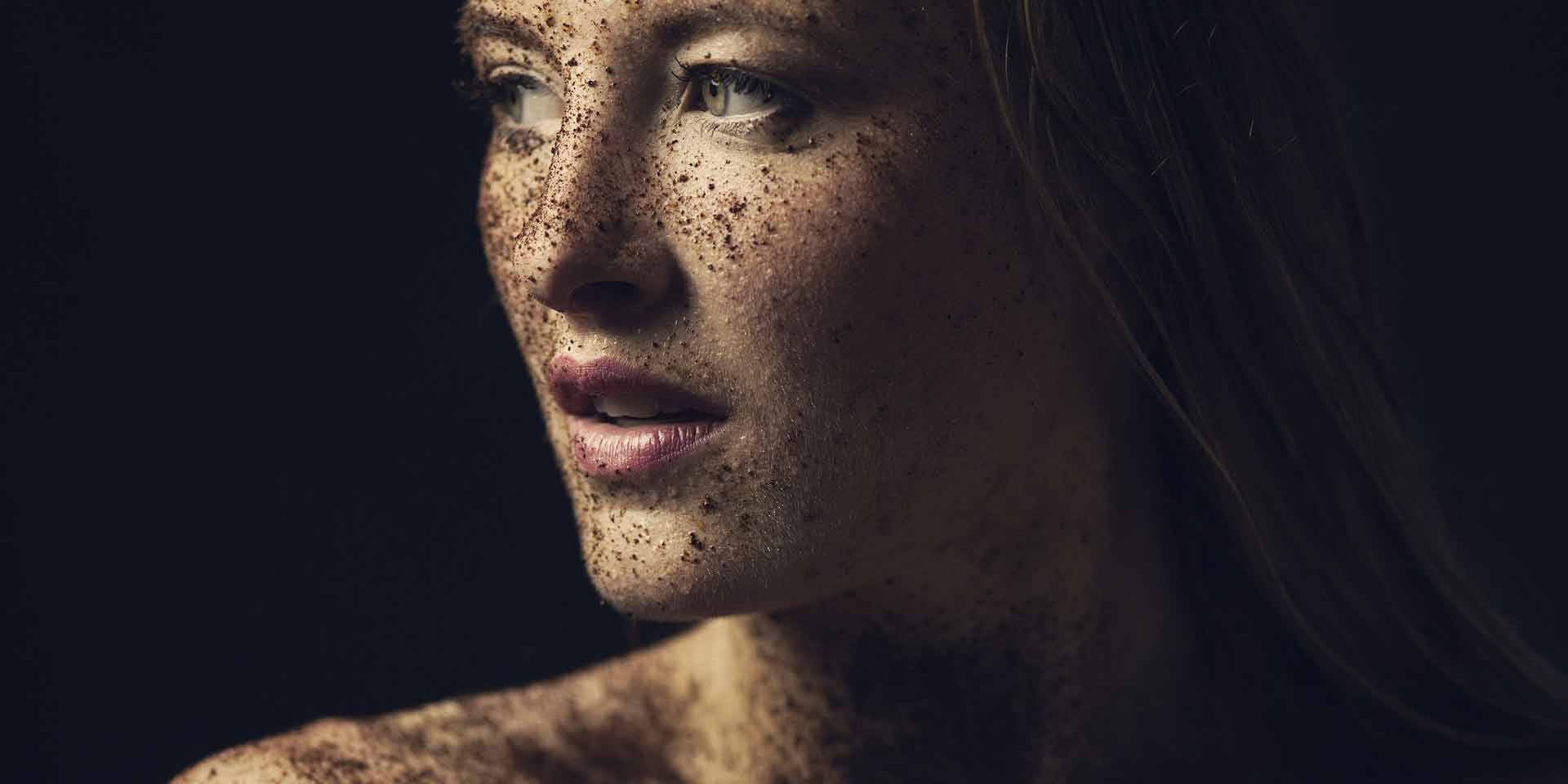 Photographie d'une femme sur fond noir, qui regarde vers la gauche, avec les épaules dénudées et la peau recouverte de terre et de poussière, afin d'illustrer le sujet de l'alimentation et vieillissement de la peau